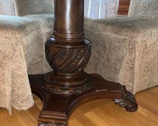 Carved Pedestal Round Dining Table — Solid wood round dining table with a carved central pedestal and scrolled tripod base, shown with six slipcovered high-back chairs. The rich dark finish and carved apron/leg details give it a traditional, formal look; pedestal construction allows generous legroom. Tabletop shows light surface wear and some small finish scuffs consistent with normal use; base carving and chair slipcovers are intact though chairs show light fabric wear. Measures roughly 48 inches diameter and standard dining height; sturdy, heavy construction will require two people to move.