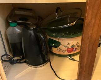 Electric Kettle Black — Compact black electric kettle with cordless base shown stored in a kitchen cabinet. The kettle is a small household model with a stainless-steel rim and power base; it appears lightly used with minor surface wear but no visible dents or cracks. Ideal for quick boiling and small kitchens; roughly fits in a cabinet shelf and stores easily with other cookware. Sold as-is without box or extras; cord and base pictured.