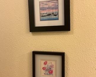 Framed Sailboat and Floral Prints — Pair of matted framed prints showing a sailboat marina scene and a floral with butterfly; each is set in a simple black wood-look frame with white double mat. Lightweight, decorative wall art suitable for hallway or bedroom; frames show minor edge wear consistent with normal use. Each frame measures approximately 12 x 10 inches overall and are ready to hang with sawtooth or wire hardware on the back.