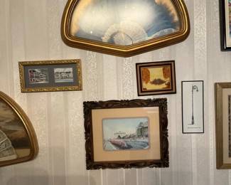 Decorative Framed Fan Shadowbox — Decorative wall-mounted shadowbox featuring a folding hand fan displayed under domed glass in a gold-tone wooden frame. The fan has a blue-to-white gradient with lace detailing and is set in a semi-circular, gilt-trimmed frame that coordinates with nearby framed prints. Overall it's a lightweight decorative piece that works well as accent wall decor in a living room or hallway. Condition is good with intact glass and frame but shows light surface wear consistent with age and display; fan appears complete with no visible tears.