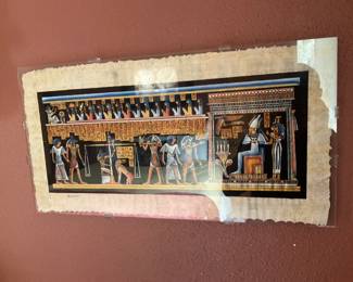 gamal Egyptian Papyrus Print — Hand-signed "gamal" papyrus print depicting a colorful Egyptian funerary scene with hieroglyphs and figures. The print is mounted under clear plastic with scalloped papyrus edges visible; colors remain bright though the papyrus shows age toning and minor edge loss. Signed lower left, it is a decorative reproduction on papyrus typical of tourist or decorative Egyptian-style art. Framed/mounted as shown; condition good with wear to papyrus edges and light surface reflections from the protective covering.