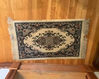 Small Oriental Wool-Blend Area Rug — Decorative small oriental-style area rug with classic medallion motif and fringed ends. Woven pile appears to be a wool-blend in cream, navy and brown tones with a detailed floral border and short hand-tied fringe. Rug measures approximately 28 inches wide by 46 inches long and lies flat — ideal as an entryway or bedside accent. Overall in good condition with light surface wear and slight fringe fraying consistent with normal use.
