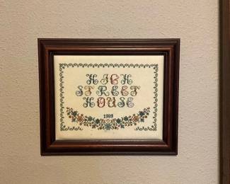 Framed Cross-Stitch Sampler 1989 — Hand-stitched framed cross-stitch sampler dated 1989 featuring an alphabet motif and floral border in muted greens, reds and blues. The sampler is mounted in a dark wood-look frame with glazed front; stitching appears intact with light age toning to the fabric. A decorative folk-style piece suitable for kitchen, hallway or cottage-style decor; frame shows minor surface wear consistent with age. Overall pleasing condition and ready to hang.