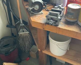 Bench Vise on Wooden Workbench — Heavy-duty metal bench vise mounted to a solid wooden workbench in a garage/workshop setting. The vise is cast-metal with an adjustable screw mechanism and shows surface wear and light surface rust consistent with regular use; it's bolted to the bench top next to a small bench grinder and typical workshop supplies. Workbench measures approximately 36 in tall, 48 in wide and 24 in deep overall; vise footprint and hardware are compact and suitable for light-to-medium clamping tasks. Condition is fair with cosmetic rust and dirt; functional parts appear intact but seller recommends cleaning and lubrication before use.