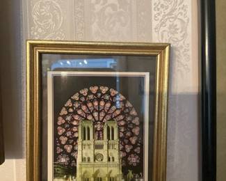 Notre Dame Cathedral Framed Print — Framed print depicting the facade of Notre Dame Cathedral with a decorative rose window motif behind it. The piece is double-matted with a black inner mat and gold wooden frame, glazed with glass. Overall framed size is modest and suitable for a hallway or gallery wall; see dimensions for exact measurements. In good condition with intact glass and frame showing light surface wear consistent with normal use.