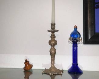 Ornate Brass Candlestick Holder — Tall ornate brass candlestick with a decorative flared base and carved foliate stem, shown with a taper candle. Solid-weight construction with detailed repoussé-style ornament across the column and base; likely late 19th–early 20th century decorative metalwork. Good vintage condition with surface patina and light oxidation consistent with age; no visible breaks or repairs. Measures tall enough for standard 12–14" tapers and makes a stately display piece for mantle or dining table.