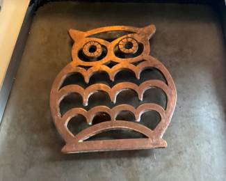 Carved Wooden Owl Trivet — Hand-carved wooden owl trivet with scalloped cutouts and stylized eyes; a decorative and functional kitchen piece for hot pans or as a tabletop accent. Solid medium-weight wood with a warm brown finish showing surface wear, light scorch marks and some edge dings consistent with use. Simple flat base sits stable on counters; measures modestly and is easy to store. Good rustic condition for use or display.