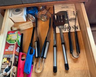 Mixed Stainless Flatware & Utensils Lot — Large kitchen drawer lot of mixed stainless flatware and cooking utensils including forks, knives, spoons in cardboard dividers plus ladles, spatulas, tongs, whisks, peelers, thermometers, long-reach lighters and other common kitchen tools. Pieces are a mix of stainless steel and plastic-handled tools showing normal kitchen wear with some minor surface scratches and light tarnish on silverplate pieces; overall serviceable for everyday use. Good assortment for stocking a household or for use as backup/party flatware; utensils are loose and not a branded matched set. Overall condition is good given age and use; see photos for exact patterns and wear.