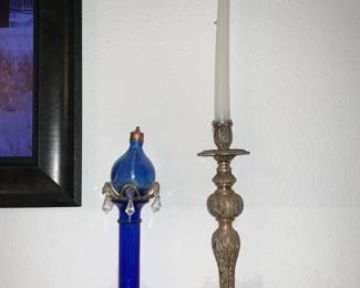 Ornate Brass Candlestick Holder — Tall ornate brass candlestick with a decorative flared base and carved foliate stem, shown with a taper candle. Solid-weight construction with detailed repoussé-style ornament across the column and base; likely late 19th–early 20th century decorative metalwork. Good vintage condition with surface patina and light oxidation consistent with age; no visible breaks or repairs. Measures tall enough for standard 12–14" tapers and makes a stately display piece for mantle or dining table.