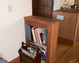 Oak Narrow Bookcase — Solid oak narrow bookcase with beadboard sides and a simple molded top, sized for magazines and small hardbacks. The piece shows light surface wear and scuffs consistent with normal use, with one lower corner showing slightly heavier wear but no structural damage visible. Compact footprint makes it useful as a room divider, end-of-sofa bookshelf, or for hallway storage; currently holds books and magazines as shown. Sturdy construction suggests solid-wood panels and traditional joinery.