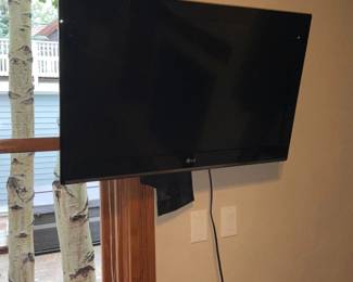 LG Flat Screen TV — LG flat-screen television shown mounted on a wall with visible LG logo on the lower bezel. The panel is a thin black LED/LCD style display suitable for bedroom or small living area mounting; power cord and wall plate visible. Screen shows light surface marks in photos but no obvious cracks; condition appears used with typical cosmetic wear. Estimated overall footprint and mounting make it an easy wall or stand swap for a small room.