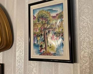 Framed Colorful Village Watercolor — Bright, colorful watercolor painting depicting a village scene with figures gathered beneath trees, matted and housed in a glossy black frame. The piece appears to be an original or print on paper with a cream double mat and a modest black wood or composite frame. Overall framed size is estimated for wall display and it's lightweight enough to hang on standard picture hooks. Condition is good with some glare on the glass visible in photos; no obvious tears or water damage to the artwork or mat observed.