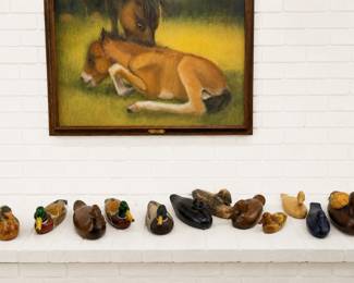 A row of wooden ducks acquired over years and years with sweet equine oil painting depicting a resting foal in a green meadow with an mom nuzzling overhead.