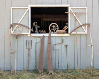 Old farm tools including a long-handled hay rake and other implements from the barn.