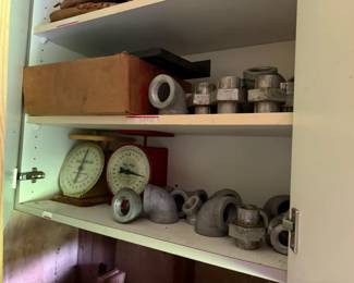 Cabinet group: two mechanical dial scales, branded oil tins, and threaded fittings