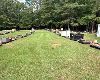 Outdoor auction scene with vehicles, equipment and appliances