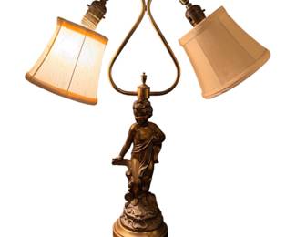 vintage figural table lamp featuring a central brass or gilt-metal cherub (putti) sculpture on an ornate round base with dual curved arms and small fabric shades