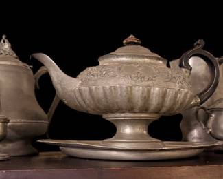 antique pewter tea and coffee service set featuring a central lidded teapot on a matching tray, accompanied by matching creamers, shakers, and lidded vessels with a rustic, aged metallic finish.