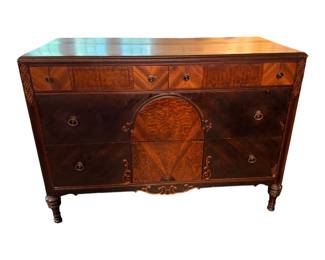 a vintage wooden dresser featuring decorative burl wood veneer, an arched central cabinet/drawer detail, and classic ring pulls.
