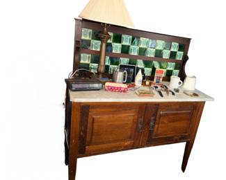 antique wooden washstand featuring a white marble top and a decorative green-and-white tiled backsplash.Early 1900’s