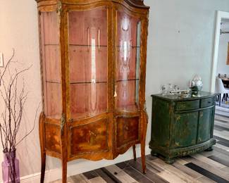 The next 5 pictures are of a French Late 19th-century Louis XV-Style Vitrine. * A serpentine (bombé) front with curved glass doors. * Ormolu (gilt bronze) mounts decorating the corners, legs, and crest. * Book-matched burl wood veneer, likely walnut or kingwood. * Hand-painted Vernis Martin-style panels on the lower doors depicting romantic pastoral scenes. * Cabriole legs and an ornate pierced crest, all characteristic of Louis XV Revival furniture.  In great overall condition!