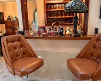 Pair of Mid-Century Swivel Bar Stools – Stylish pair of vintage swivel bar stools featuring tufted brown vinyl upholstery, chrome pedestal bases, footrests, and adjustable-height design. A great addition to a home bar, game room, or retro-inspired kitchen. Contents in the background sold separately unless noted.