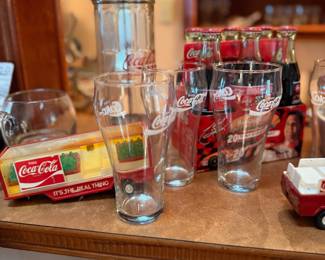 Coca-Cola Glassware & Collectibles – Collection of Coca-Cola memorabilia featuring collectible drinking glasses, commemorative glass bottle sets, a vintage-style Coca-Cola dispenser, and assorted advertising collectibles. Perfect for Coca-Cola collectors, home bars, or retro Americana displays. Sold individually unless noted.