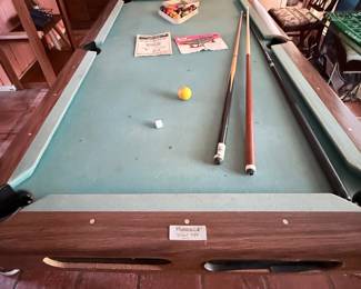 Brunswick Windsor VIP Model GK Billiard Table – Quality Brunswick pool table, Model GK, featuring a wood-grain finish, leather-style drop pockets, and green felt playing surface. Includes the original Brunswick owner's manual, billiard balls, cue sticks, chalk, triangle rack, and additional accessories shown. A classic table from one of the most respected names in billiards, perfect for a game room or recreation space. Sold as found.