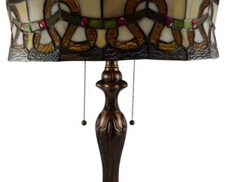 184 - Tiffany Style Stained Glass Table Lamp 24" (Description): A Tiffany style stained glass table lamp featuring a decorative domed shade with Art Nouveau inspired scrollwork pattern. The shade incorporates panels of amber, cream, green, and clear textured glass accented with red glass cabochons. The lamp sitsatop a cast metal base with a bronzed finish and classical foliate design. Dual pull chain operation. Electric/electronic/mechanical item - No