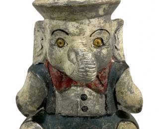 2394 - Elephant Statue 12" tall (Description): A charming elephant statue measuring 12 inches tall. The seated elephant figure is dressed in a jacket with a red bow tie and wears a domed hat. The piece features painted details with an aged, weathered patina and glass eyes.