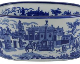 175 - Small Blue & White Transferware Planter (Description): Small blue and white transferware planter featuring a scenic design with architectural elements, figures on horseback, and pastoral village scenes. The oval vessel has twin handles on either side and a cobalt blue rim. Measures 5 1/2" x 13" x 9".