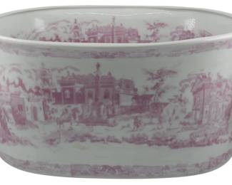 174 - Large Pink & White Transferware Planter (Description): Large pink and white transferware planter featuring scenic European architectural and landscape designs in a traditional toile pattern. The oval vessel has twin handles on either side and displays classical buildings, figures, and pastoral scenes rendered in pink transfer print on a white ceramic body. Measures 8.5" x 18" x 13".