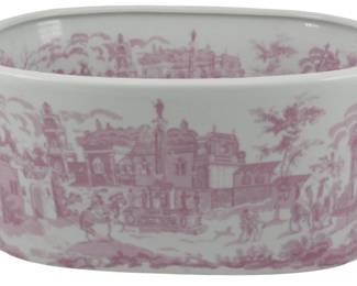 173 - Small Pink & White Toile Ceramic Planter (Description): Small pink and white ceramic planter featuring a toile-style transferware design depicting a pastoral European village scene with architecture, figures, horses, and carriages. The oval-shaped planter has two handles on either side and a rolled rim.Measures 5 1/2" x 13" x 9".