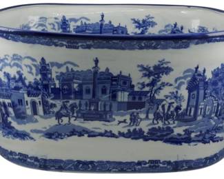 176 - Large Blue & White Transferware Planter (Description): Large blue and white ceramic planter or cachepot featuring transferware decoration in a scenic pattern. The oval vessel is adorned with detailed landscape vignettes depicting architectural scenes with figures on horseback, buildings, and trees in the classic blue and white palette. The planter features pierced handles on either end with cobalt blue accents and decorative banded borders along the rim and base. Measures 8