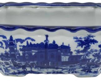 106 - Blue & White Porcelain Planter 4.5"x12"x6" (Description): Blue and white porcelain planter featuring a traditional transferware-style scenic design depicting architectural buildings and landscape elements. The rectangular vessel has a scalloped rim with cobalt blue edging and twisted rope-style handles oneach end. Rests on four decorative feet. Measures 4.5 inches tall by 12 inches long by 6 inches wide.