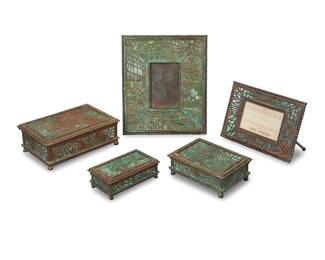 1246 Five Tiffany Studios bronze and Favrile glass 'Pine Needle' desk items Early 20th century Verdigris patinated, comprising two lidded boxes, a stamp box, an easel-back picture frame, and an easel-back calendar holder Each impressed: TIFFANY STUDIOS / NEW YORK; smaller box numbered: 800; stamp box numbered: 801 5 pieces Frame aperture 3 3/8 x 2 1/4 in.; height of largest box 2 1/4 in., width 6 in., depth 4 1/8 in. Estimate: $700 - $900