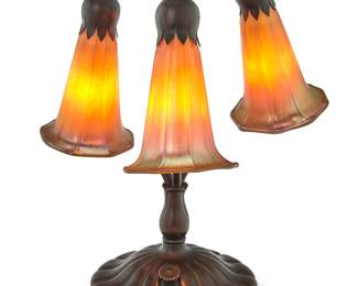 1247 A Buffalo Metal Works Tiffany-style lily lamp 1976 The patinated copper alloy base issuing three lights, each with iridescent gold glass lily-form shade, electrified Incised with date to underside of base: Buffalo Metal Works / #138 / 5-76 Height 12 1/2 in., diameter 10 in., irregular Estimate: $500 - $800