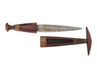 1429 An Ovambo dagger with sheath Late 19th/early 20th century; Angola/Namibia Each in carved dark wood with copper and wrapped wire accents, featuring a tapered ridged metal blade set in a carved wood handle, with a matching sheath with wide top handle and integral wooden channel for a cord attachment Initials marked to sheath end edge: GL 2 pieces Overall height 12 in, width 4 1/8 in., depth 1 1/4 in.; knife height 11 1/2 in., sheath height 7 1/2 in. Estimate: $1,000 - $1,500