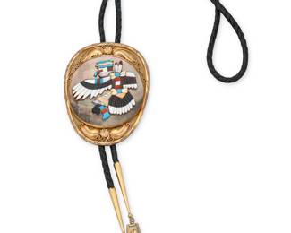 1326 Wilson Yazzie (20th century, Diné [Navajo]) & Sarah McCray (20th century, Diné [Navajo]) A large Zuni-style 12k gold-plated sterling silver Eagle Dancer pictorial bolo featuring a central multistone sculptural overlay Katsina dancer figure in mother of pearl, jet, turquoise, coral, and other shells, all applied to a set round abalone shell disc, bordered by 12K gold plated applied wire and feather accents, and mounted on a black braided leather cord with gold-plated tips and overlay dangles Etched in script verso: Bolo by Wilson Yazzie / Carving by Sarah McCray /12k-GF on Sterling Bolo 3 1/8 x 4 1/8 in., cord (including dangles) 40 in. 114.5 grams gross Estimate: $300 - $500