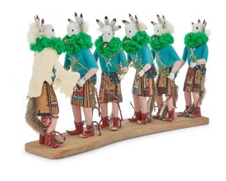 1025 Nancy Kee (20th century, Diné [Navajo]) A Diné (Navajo) Yei Bi Chei procession Depicting five figures and a talking god, in carved polychromed wood with yarn and fur accents, all mounted to a wood base Signed and inscribed on the underside "Nancy Kee / Yei ba chai" Height 10 1/4 in., width 20 in., depth 4 1/4 in. Estimate: $300 - $500