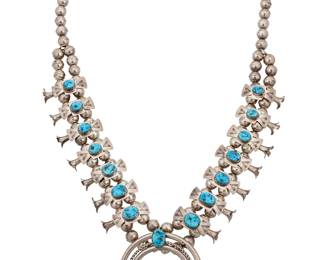 1320 A Diné (Navajo) or Zuni 'Box & Bow' squash blossom necklace Late 20th/21st century With fourteen stamped sterling silver 'box and bow' blossoms, each with graduated set turquoise, and a central set turquoise three-wire naja, all set to a double strand of silver beads Stamped: LK / Sterling 27 1/2 x 2 3/4 in. 154.0 grams gross Estimate: $800 - $1,200