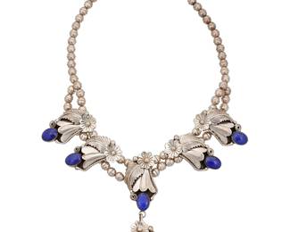 1397 A Southwest sterling silver and lapis lazuli squash blossom necklace A small squash blossom-style necklace with five ornate blossoms with set lapis lazuli, suspending a matching pendant, all on a double strand of silver beads Stamped: A / Sterling 20 1/4 x 4 in. 70.0 grams gross Estimate: $500 - $700