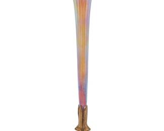 1197 A Tiffany Furnaces Favrile glass and gilt-bronze vase Early 20th century The spreading foliate base mounted with an iridescent glass trumpet vase Impressed to underside: ['L' in cartouche] / LOUIS C.TIFFANY FURNACES.INC. / FAVRILE / 158 Height 17 1/4 in., diameter 5 1/2 in. Estimate: $700 - $1,000