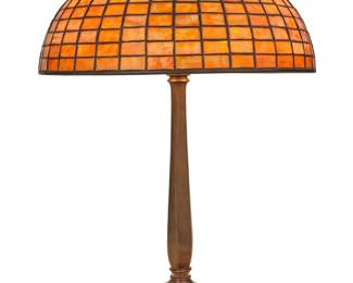 1194 A Tiffany Studios Favrile glass geometric table lamp Circa 1902-1919; New York, NY The caramel-colored leaded glass geometric shade with square brick pattern on a three-light patinated bronze base, electrified Shade marked in relief: Tiffany Studios / New York / 1486; base unsigned Height overall 22 1/2 in.; height of shade 7 in., diameter 16 in. Estimate: $6,000 - $8,000