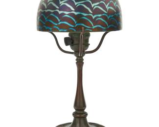 1099 A Tiffany Studios boudoir lamp and glass shade Early 20th century with later shade The patinated bronze base issuing a single light and three arms surmounted by a later reproduction iridescent pulled feather glass shade, electrified Base impressed: Tiffany Studios / New York / 322; incised: 958 [indistinct]; shade unmarked Height overall 14 3/4 in.; height of base 11 in., width 7 in., depth 5 1/2 in.; height of shade 4 3/4 in., diameter 7 1/2 in. Estimate: $800 - $1,200