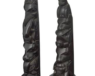 1137 Two carved model totem poles Early 20th & late 20th century Comprising a Haida carved argillite totem pole featuring an eagle above two figures eating fish and a seal, one likely a bear, and one an orca; together with a later black resin reproduction totem with various animal figures including a raven, a frog, and possible an orca The resin marked: REP 2 pieces Stone height 9 in., width 2 3/4 in., depth 2 3/4 in.; resin height 10 1/4 in., width 2 1/4 in., depth 2 in. Estimate: $800 - $1,200