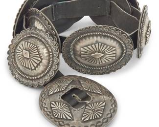 1318 A Southwest sterling silver concha belt Mid/late 20th century With a chunky sterling silver oval buckle and nine oval conchas, each with silver overlay and stampwork to edges, each concha lined with black leather, and all mounted to a black leather strap Stamped with unidentified crossed hourglass mark Buckle 3 1/4 x 4 in.; each concha 2 3/4 x 3 1/2 in.; strap 35 x 1 1/8 in. 780.8 grams gross Estimate: $1,200 - $1,800