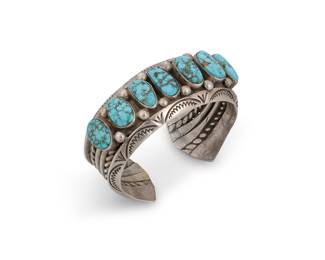 1370 A Diné (Navajo) sterling silver and turquoise cuff bracelet Mid-20th century A heavy cuff of stamped carinated, rounded and twisted wire supporting seven set turquoise stones with silver drop accents and hammered flared terminals Unmarked 6 1/8 in. total inner C x 1 3/8 in., including a 3/4 in. gap 103.8 grams gross Estimate: $800 - $1,200
