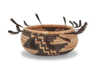 1162 A Pomo gift basket Mid/late 20th century; Northern California The coiled small oval bowl with a diagonal stepped zigzag motif to each side and quail top knot feathers to the rim Height 2 in., width 4 3/8 in., depth 3 3/8 in. Estimate: $500 - $700