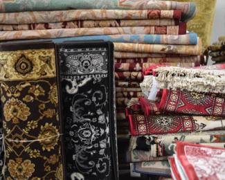 Large assortment of folded and rolled rugs featuring traditional patterns, rich colors, and varied designs.